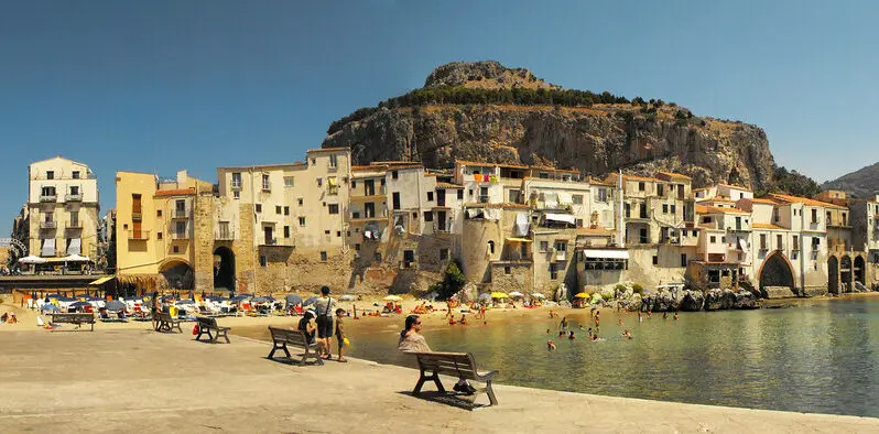 Veduta de Cefalù, in una giornata estiva. In mare, vicino la spiaggia, gente che si ristora con un bagno rinfrescante.
