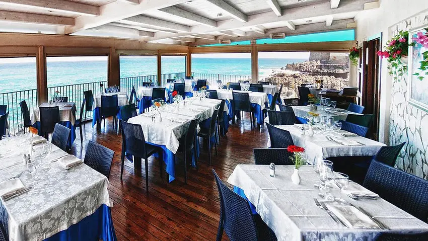 Sala del ristorante sul mare Kentia, un altro dei fantastici ristoranti dove mangiare a Cefalù. La sala è arredata in modo classico, ed i colori delle sedie richiamano il blu del mare visibile appena fuori dalla veranda.