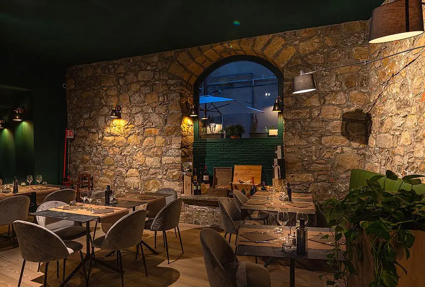 La bellissima sala interna di Braceria Italiana Fuorimondo, davvero uno dei migliori locali dove mangiare a Cefalù. Le parti con pietre a vista si sposano perfettamente con lo stile moderno dato dai colori neutri di tavoli e sedie.