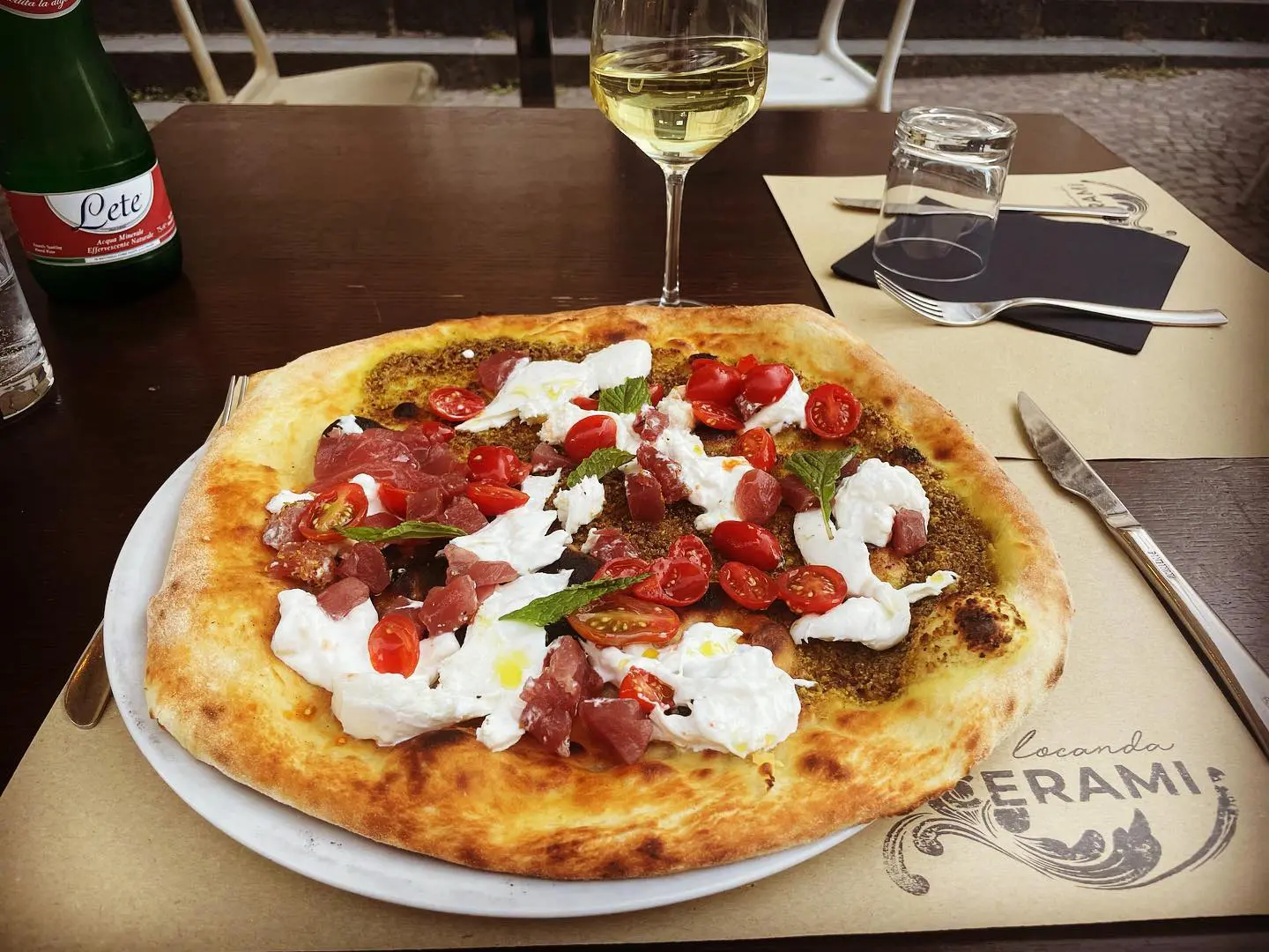 Pizza su un piatto, pizza con stracciatella, pomodorini, tartare. È una delle ottime pizze di Locanda Cerami, il logo è presente sulla tovaglietta.