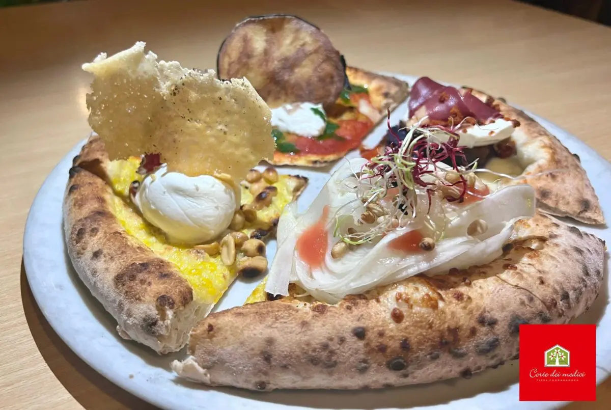 Una fantastica pizza gourmet, con presentazione stellata e molto riccamente condita. Siamo da Corte dei Medici a Catania. Logo del locale in basso a destra.