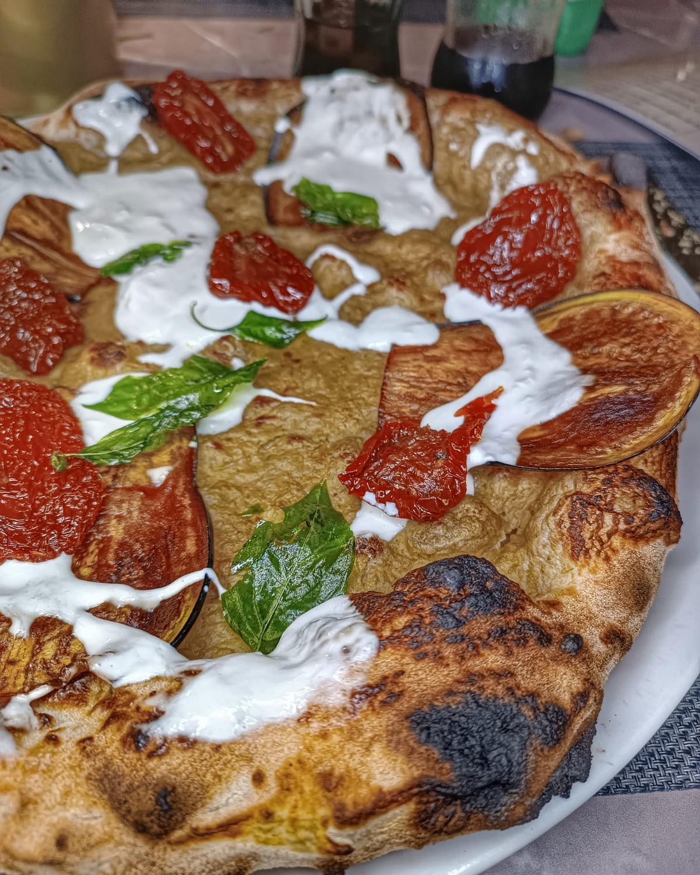 Particolarissima pizza focaccia vista da vicino, con stracciatella e pomodori chiaramente visibili, e intere foglie di basilico. 