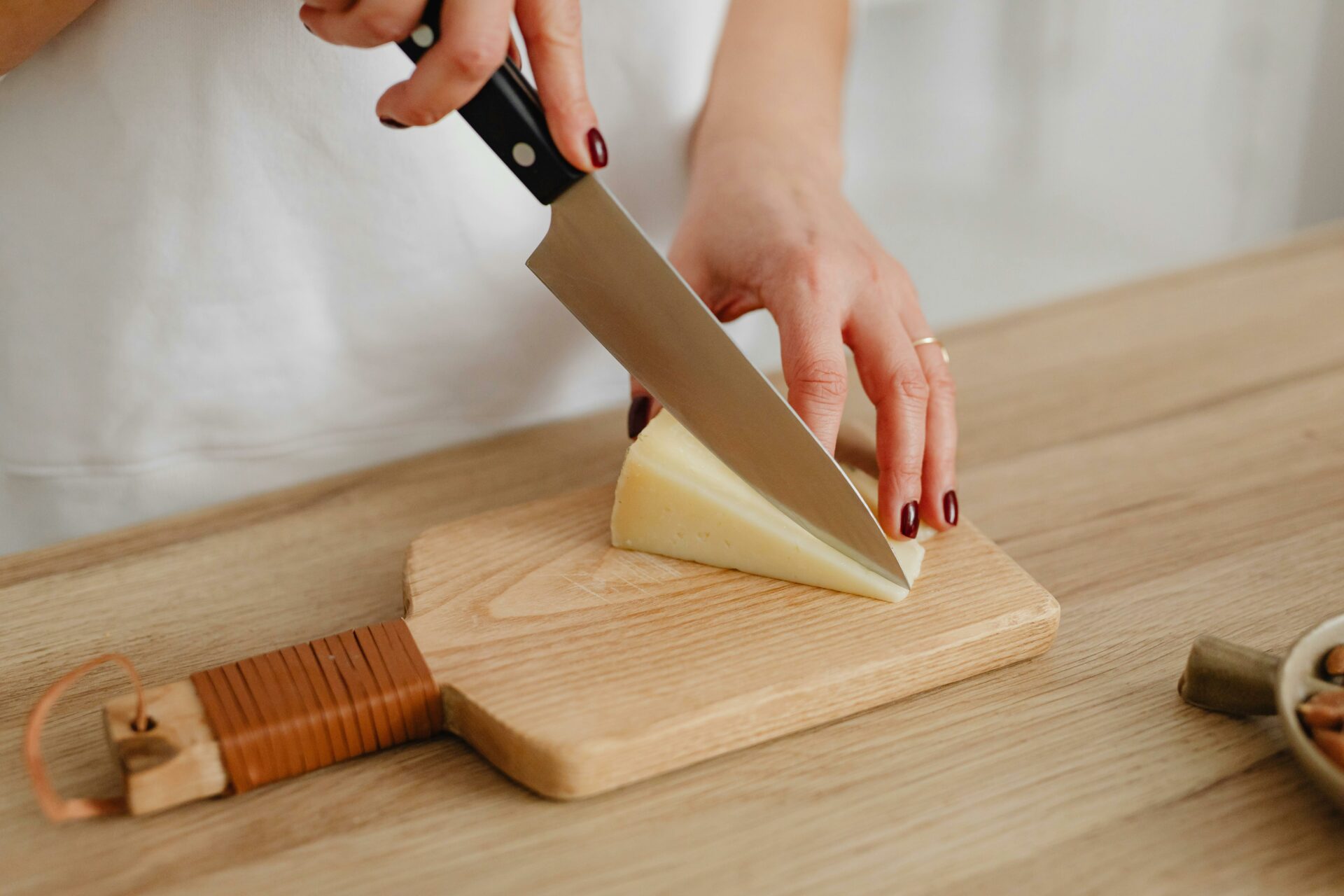 migliori coltelli per formaggio, coltello, tecniche di taglio del formaggio, mano che tiene un coltello per tagliare del formaggio, tagliere 